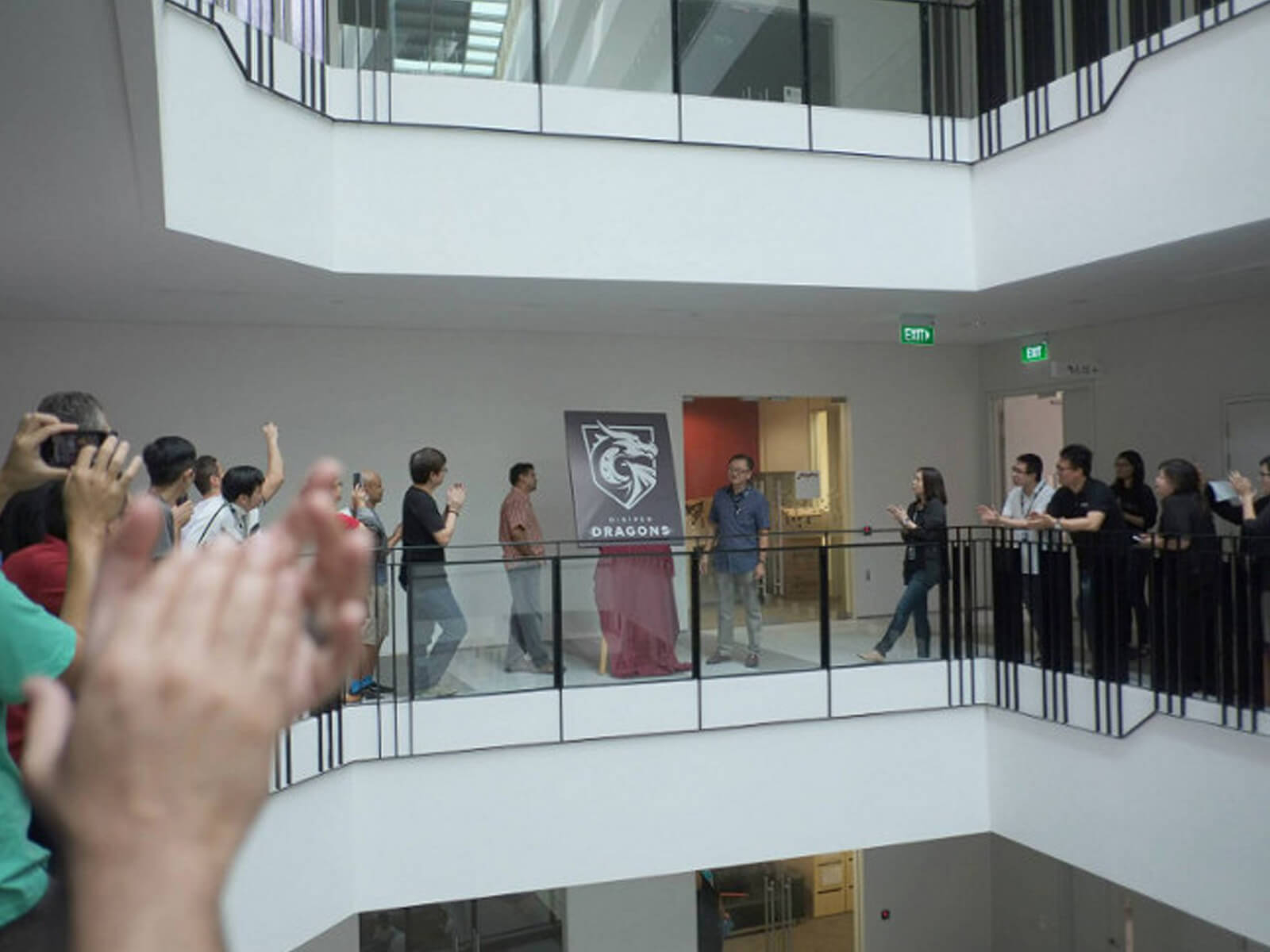 People on the second floor applaud the unveiling of a poster depicting the DigiPen Dragons logo