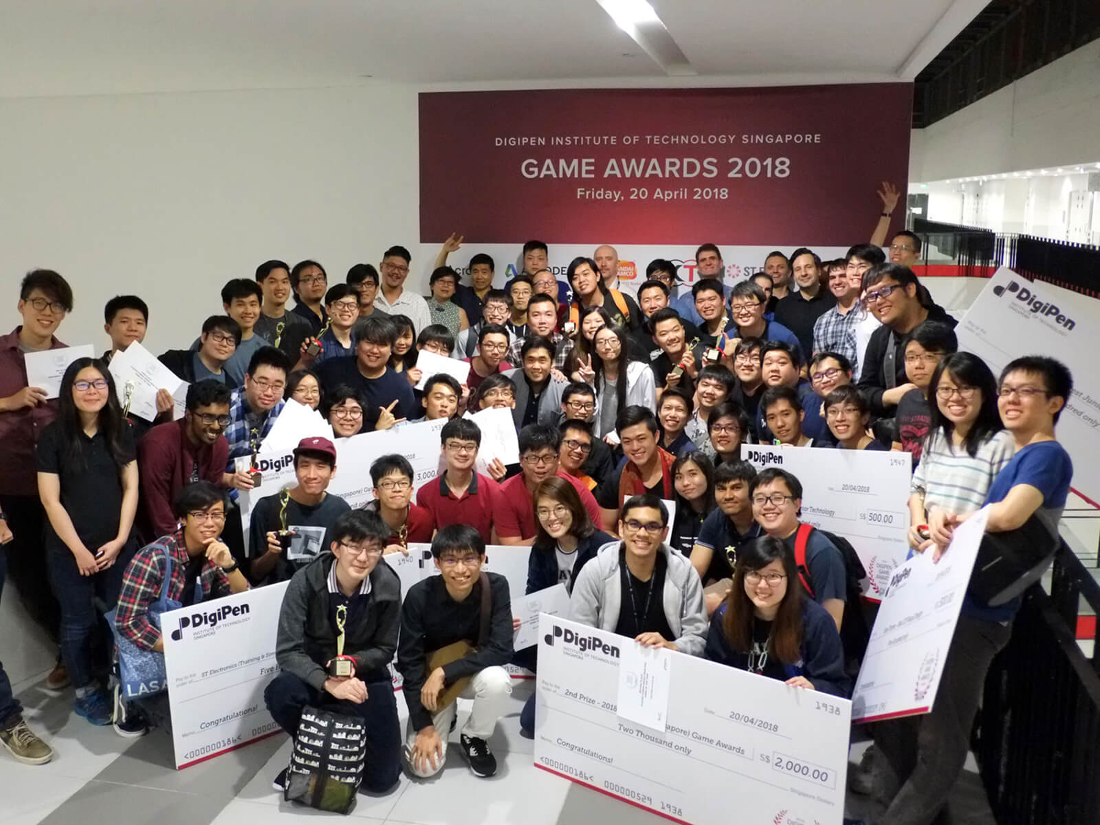 Participants in the DigiPen (Singapore) Game and Animation Awards pose, with award-winners holding giant novelty checks up front