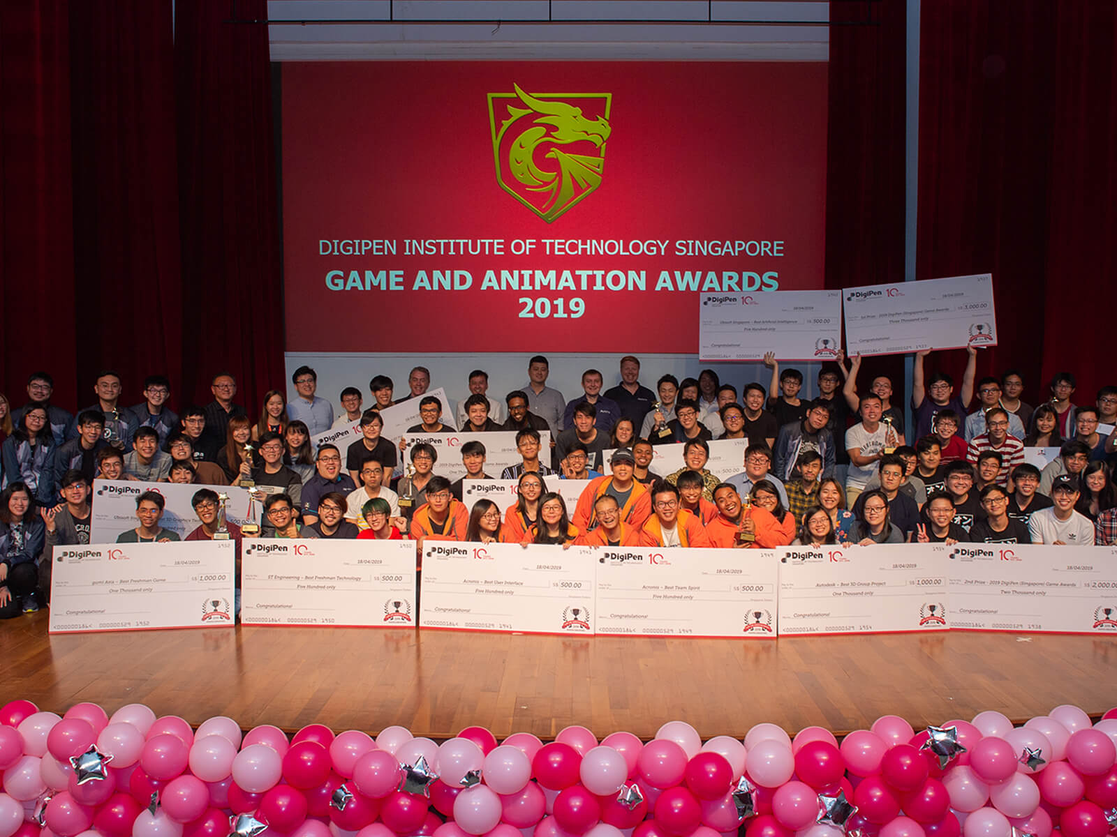 Four rows of students line up on stage to display their giant prize checks during the 2019 DigiPen Game and Animation Awards ceremony.