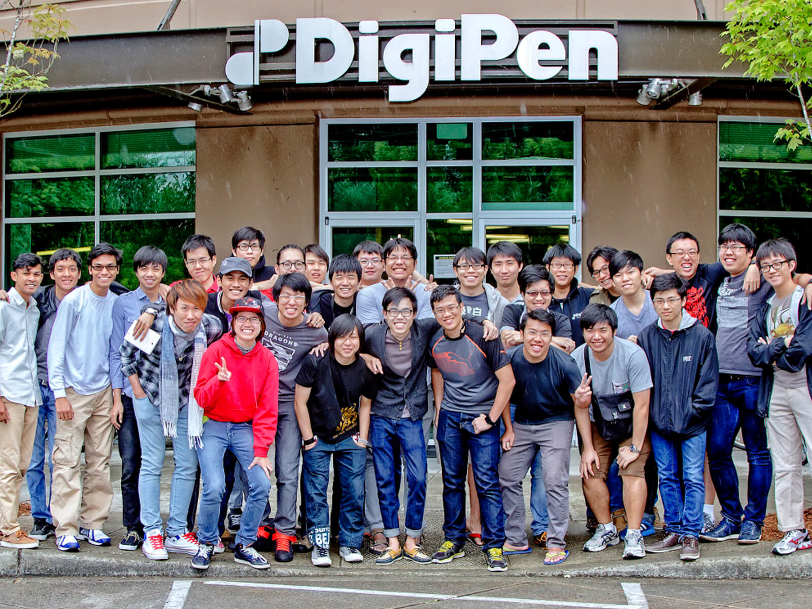 Dozens of students pose for a picture in front of a building with the DigiPen logo and name above the door