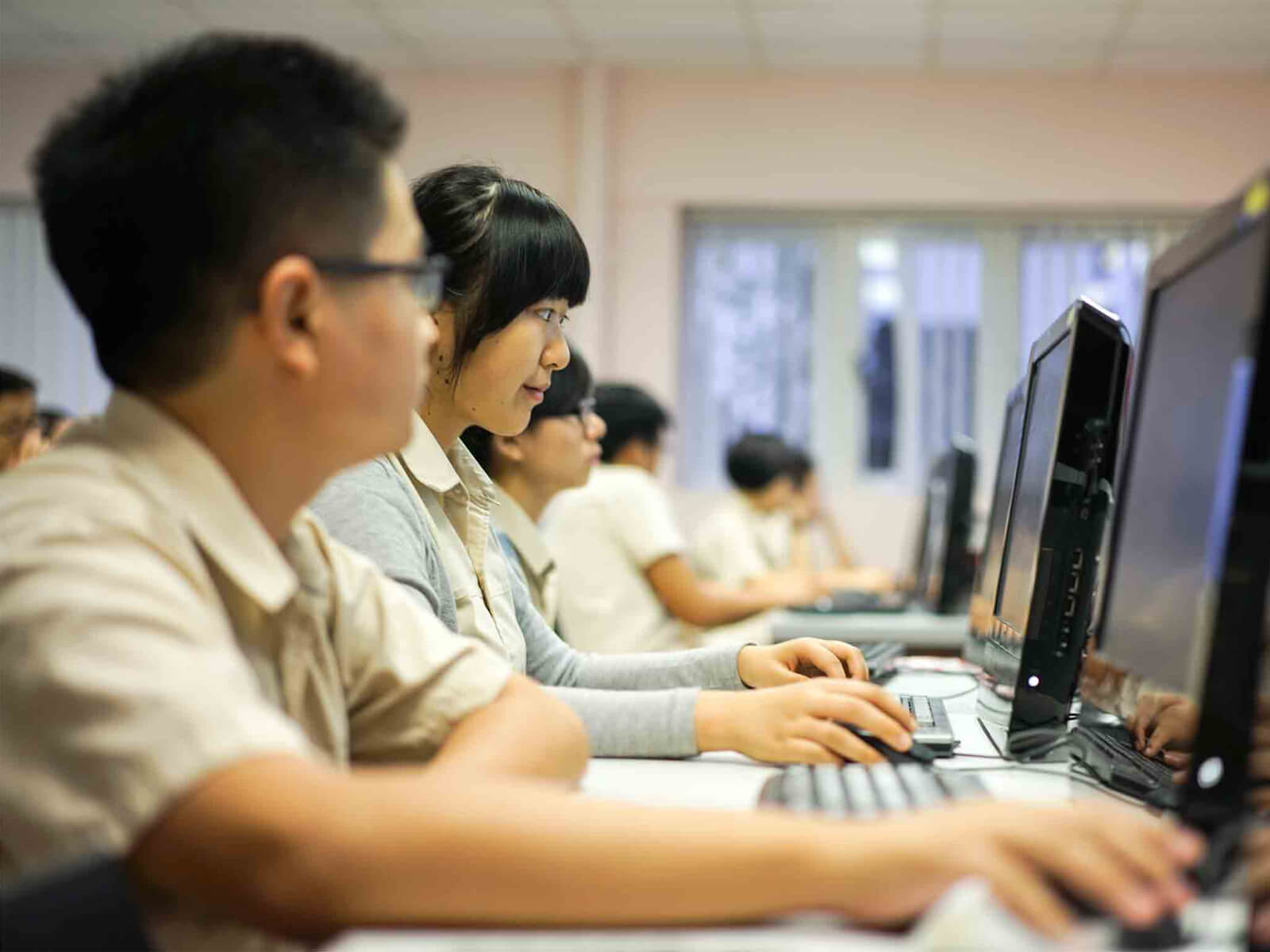 Students sit at a desk looking at a computer monitor while using a mouse and keyboard