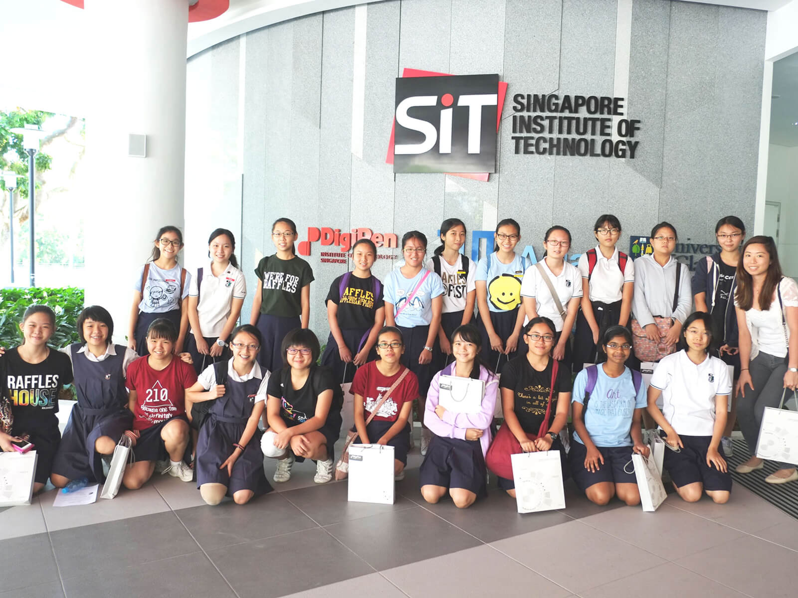 A group of schoolchildren pose for a picture in front of a building displaying the Singapore Institute of Technology logo