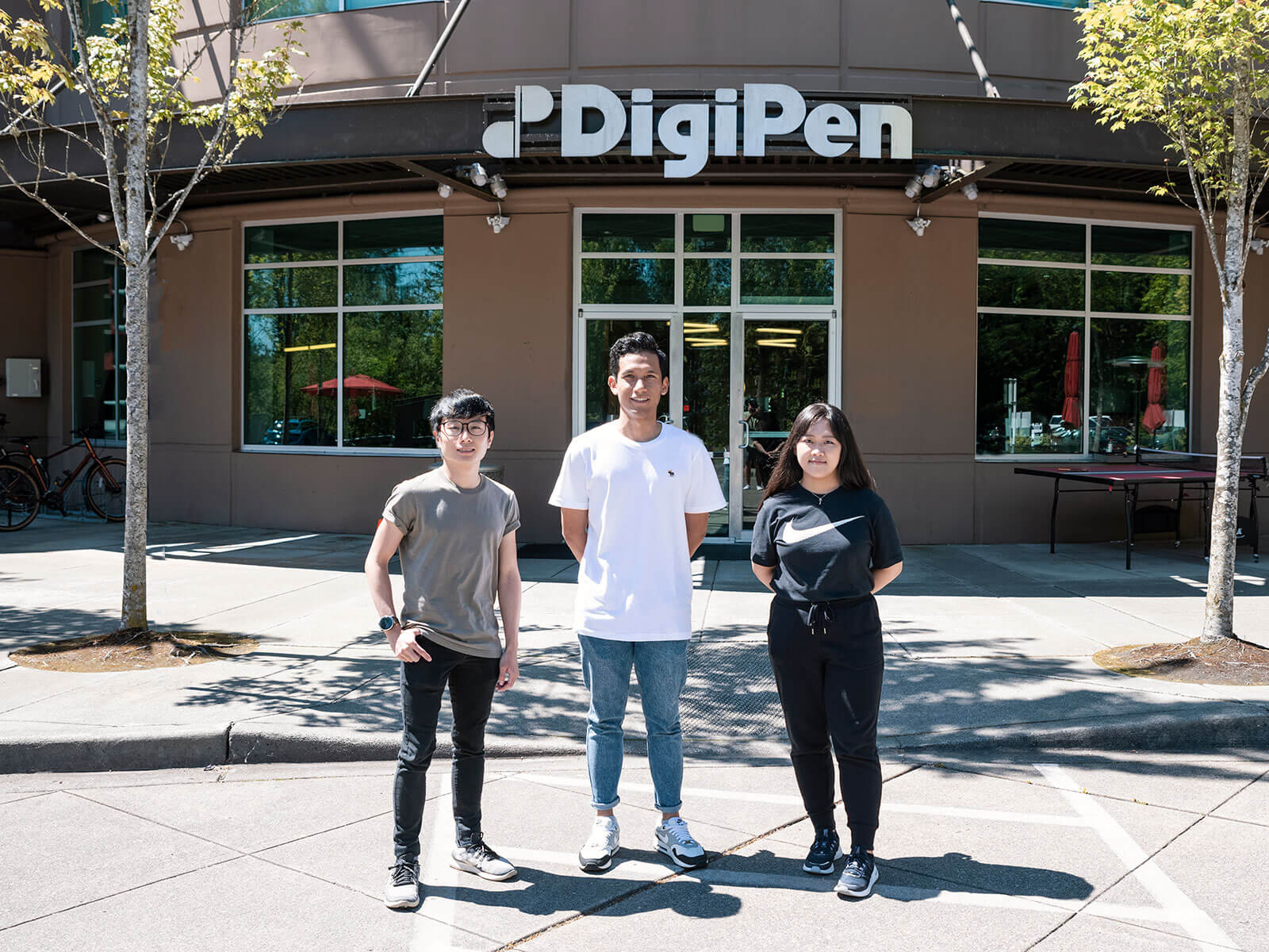 Three OIP students stand in front of the main doors of the DigiPen Redmond campus.