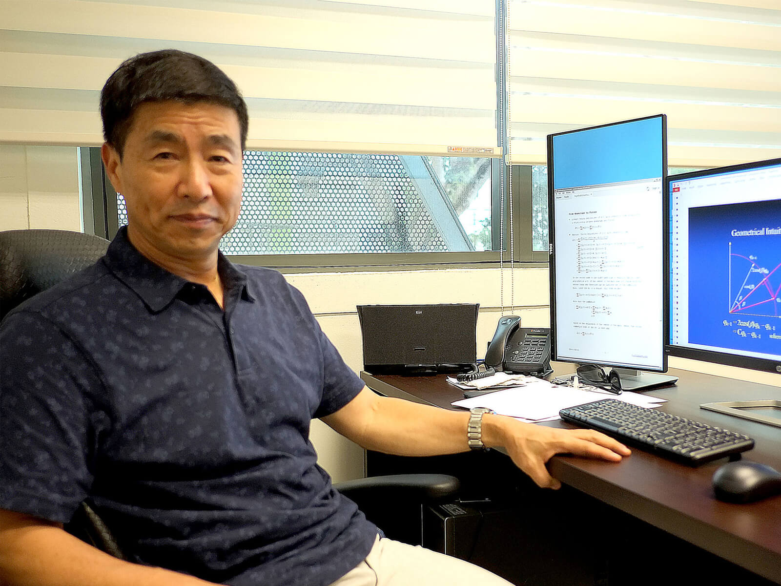 Dr. Xin Li poses for a photo at his desk which has one vertical and one horizontal monitor