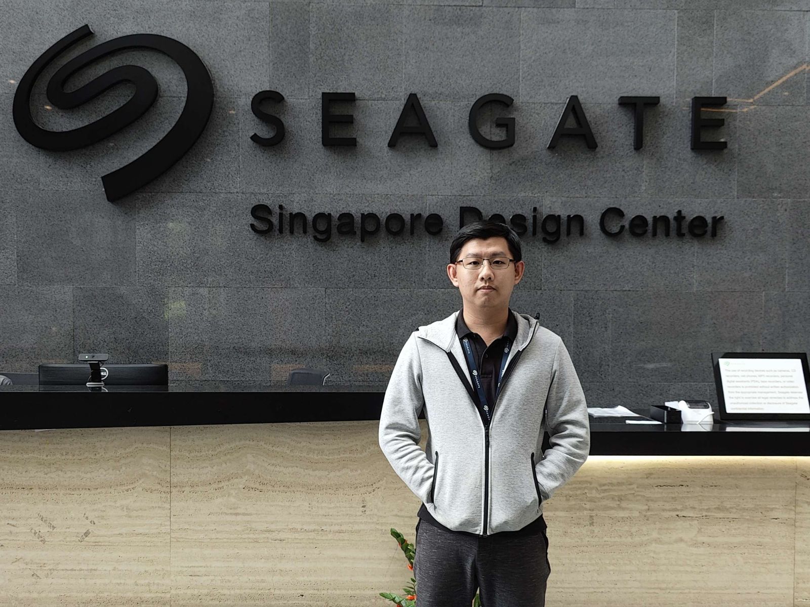 DigiPen Graduate Toh Yu Xing stands in a building's lobby with the SEAGATE logo behind him