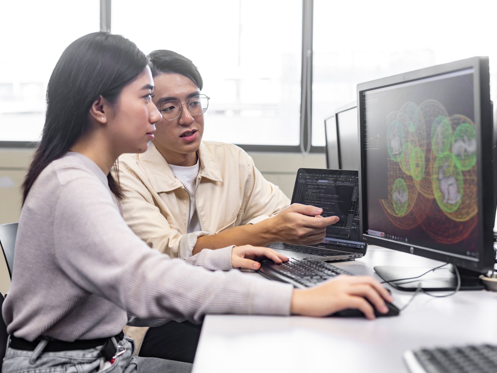 A professor sits next to a student in front of a computer.