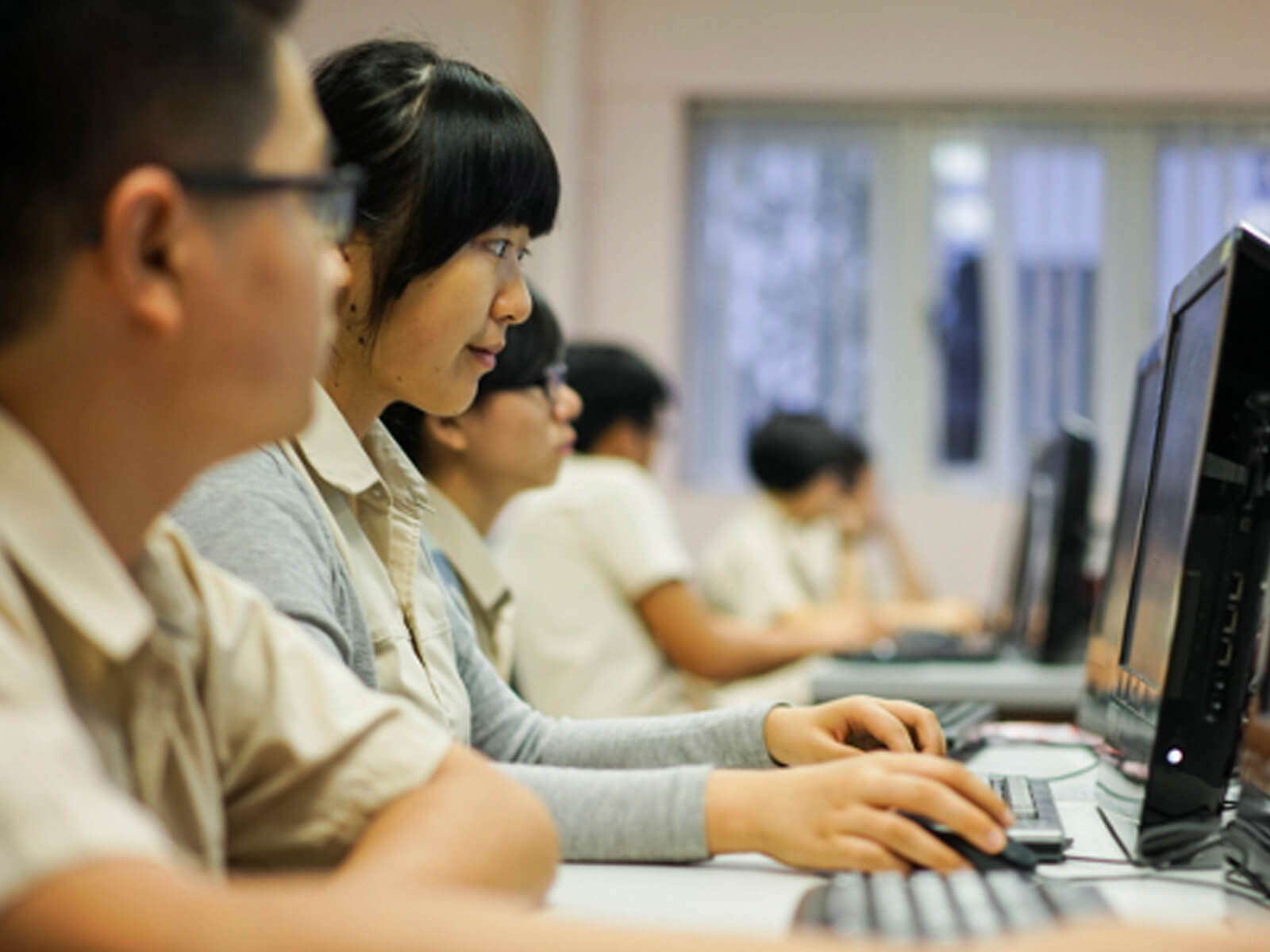 A student, seen from the side, looking at a computer monitor and working with a mouse and keyboard