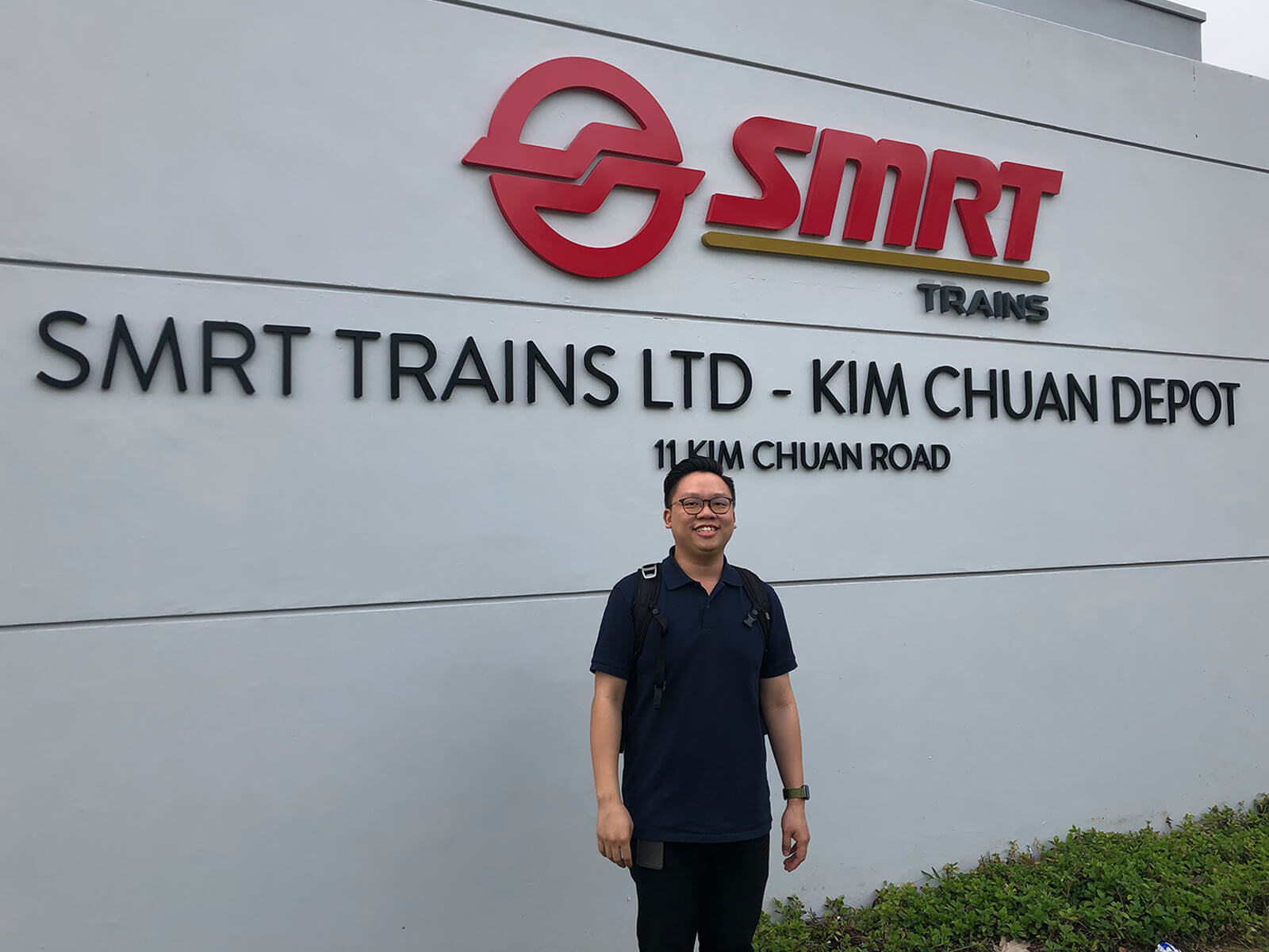 Samuel Tan stands in front of the ‘SMRT Trains Ltd. - Kim Chuan Depot” sign.