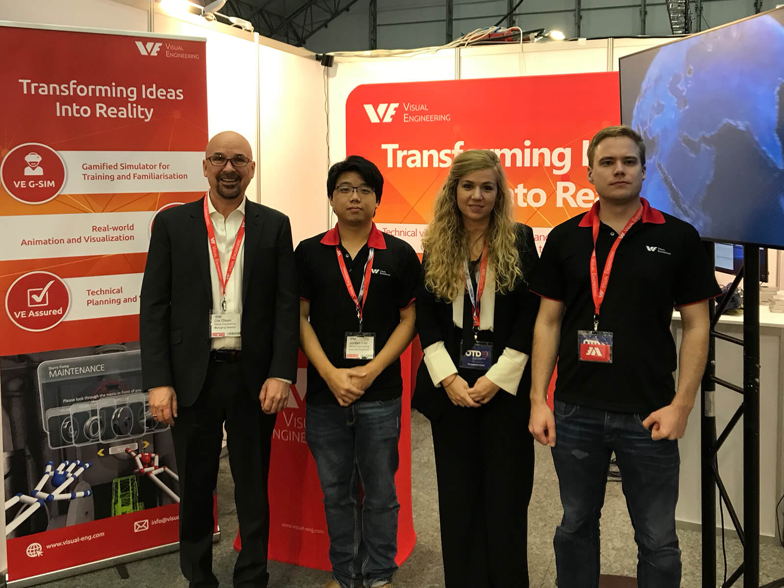 4 Visual Engineering employees stand parallel together facing camera in front of a company booth at an expo event.