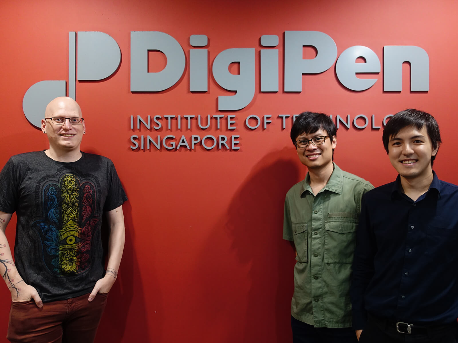 Kevin Prior, Howard Sin, and Gerald Wong stand in front of a red wall with the DigiPen Institute of Technology Singapore logo