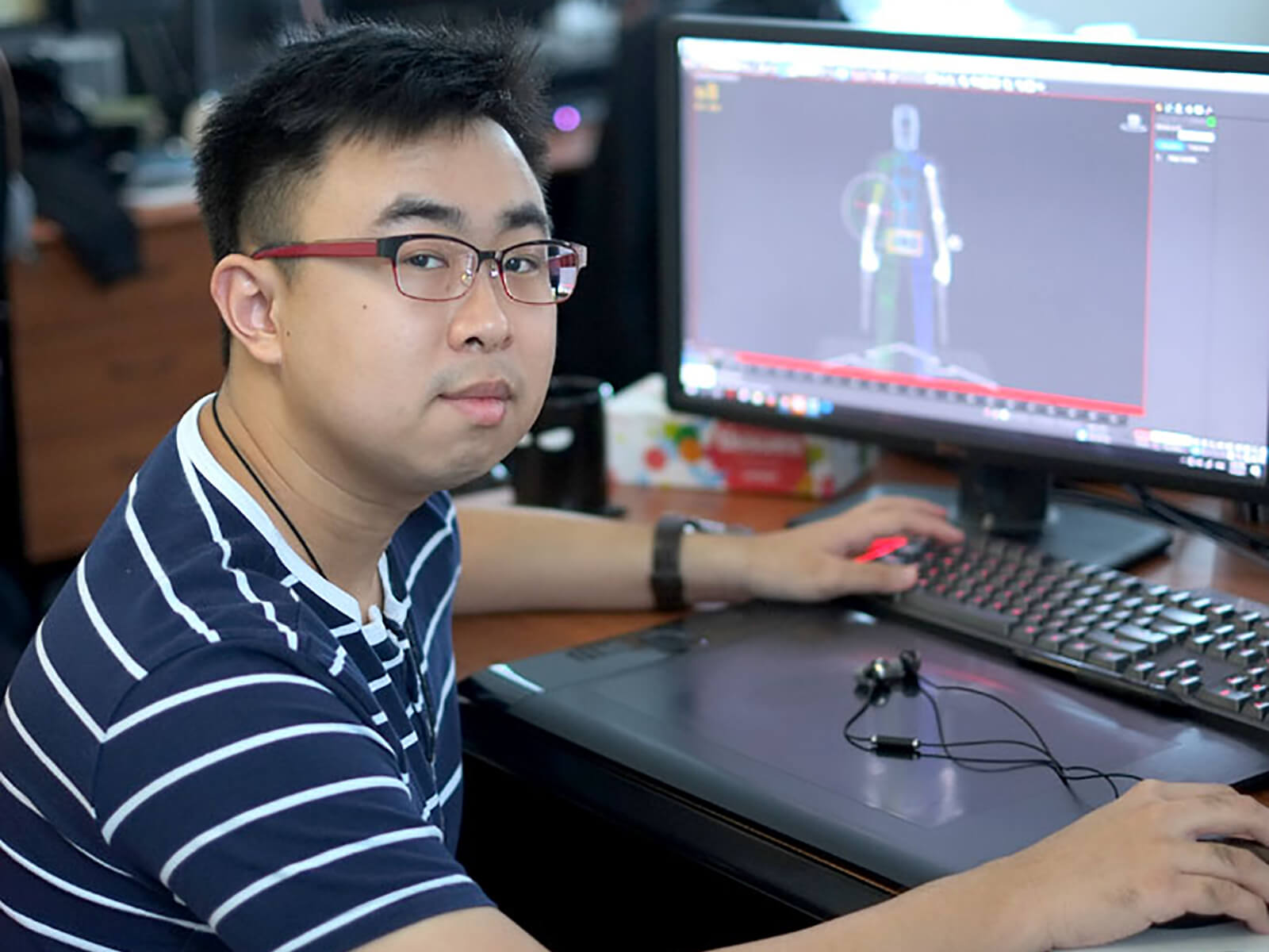 DigiPen graduate Lauri Gui poses for a photo at a desk with a monitor and tablet