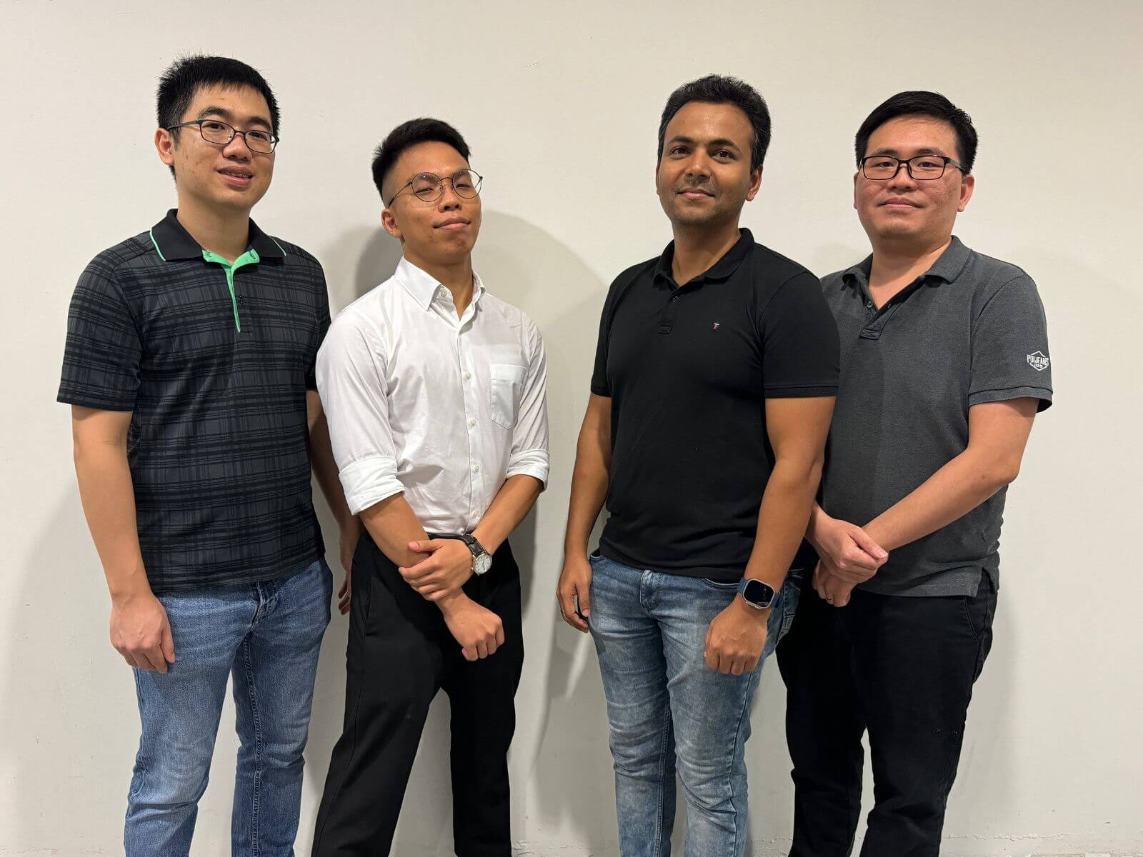 Four male students standing in front of a wall.