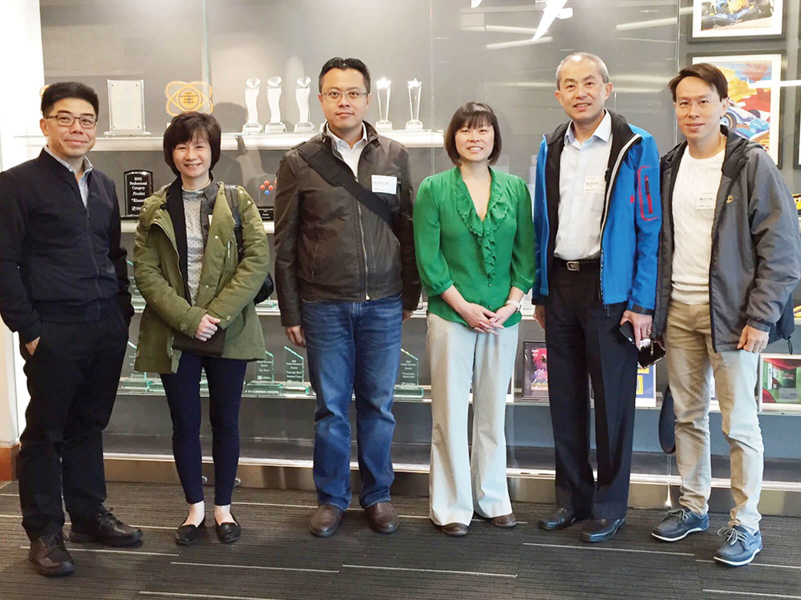 Visitors from Ngee Ann Polytechnic pose for a photo in front of a display case of DigiPen awards and project posters