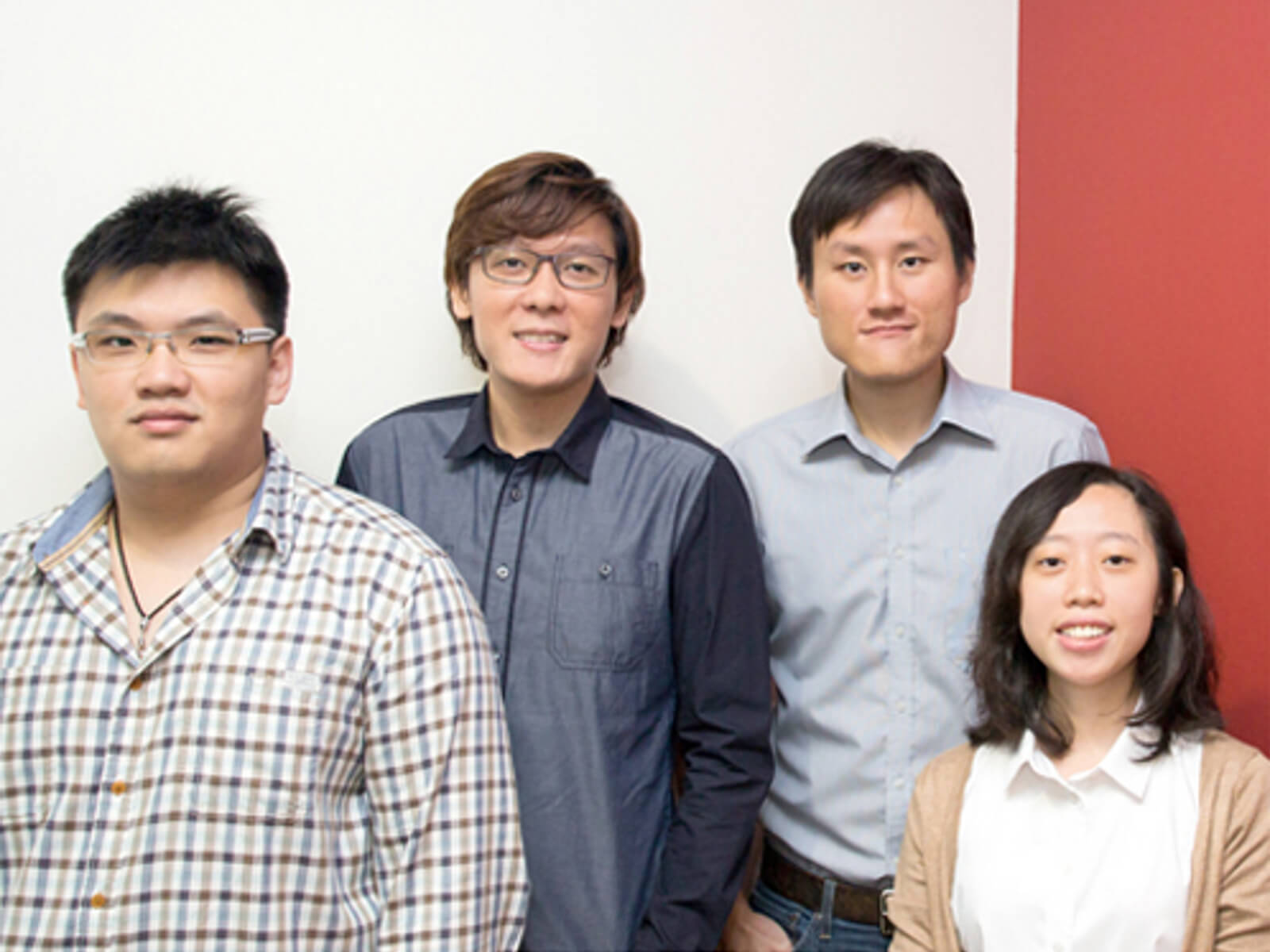 Four DigiPen (Singapore) graduates pose for a photo against a white and red wall