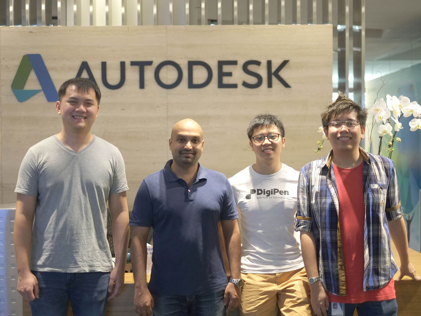 DigiPen graduates pose for a photo with Autodesk logo on a beige wall behind them