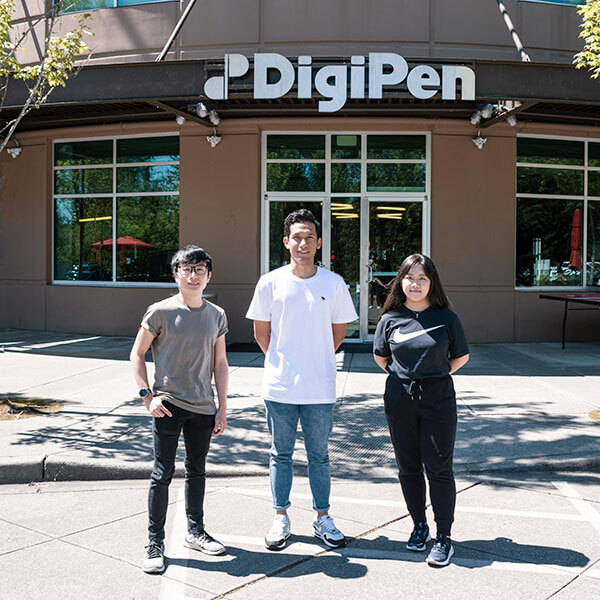 Three OIP students stand in front of the main doors of the DigiPen Redmond campus.