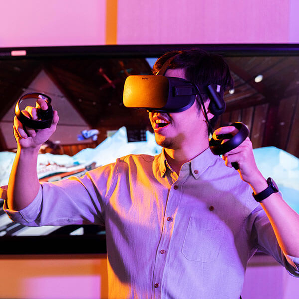 A male student wears VR goggles while holding a controller in each hand
