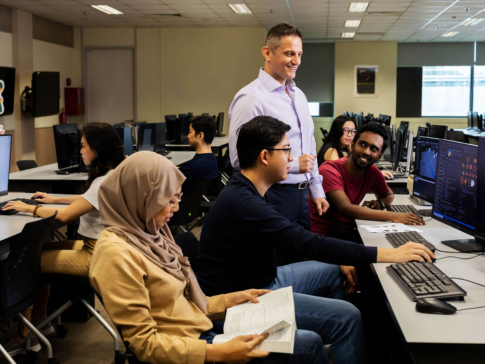 A DigiPen Singapore instructor stands and looks at a computer surrounded by students