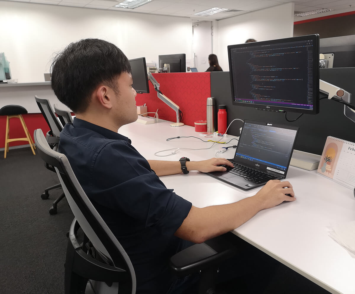 SIT-DigiPen (Singapore) graduate Alan Lim sits at a long desk with laptop and monitor.