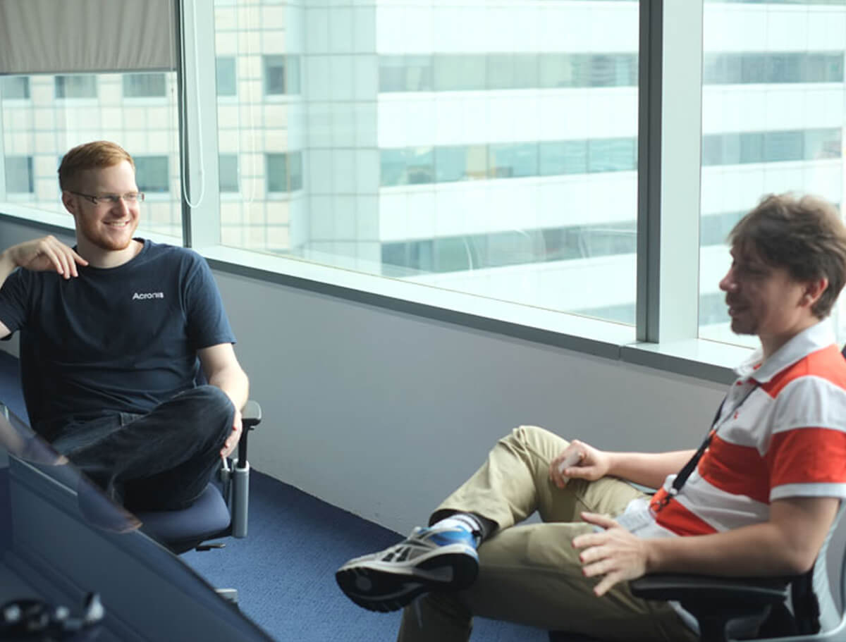 DigiPen graduate Alan Miller sits in a chair across from Vitaly Pogosyan, a window looking out to another building is behind