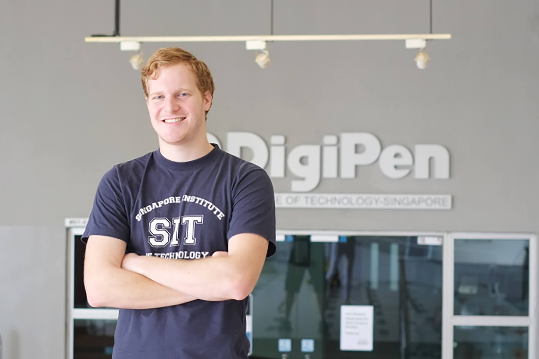 RTIS student Alan Miller poses for a photo arms crossed in front of a building. DigiPen logo is on the building behind him.