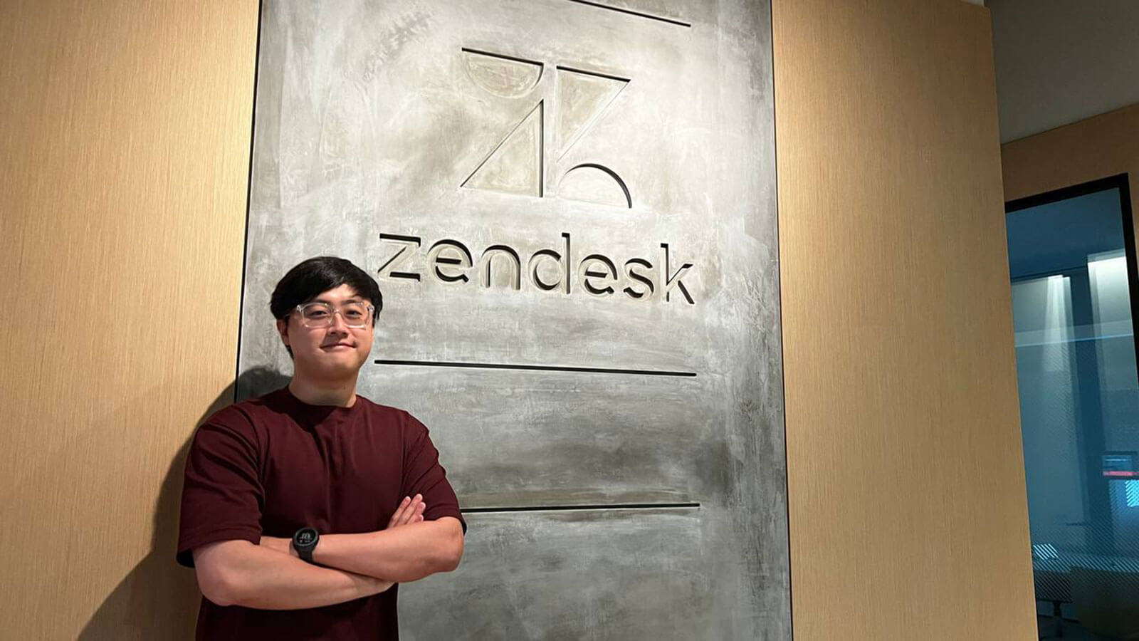 Alumnus Lim Kay Hwee poses in front of a Zendesk logo sign.