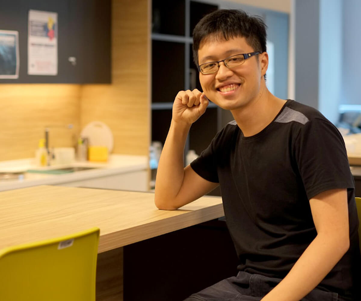 DigiPen graduate Chin Jia Hao smiles sitting at and resting his elbow on a desk