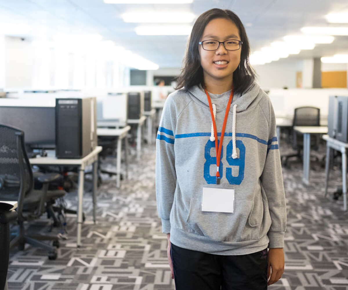 NUS High student Chin Tian poses for a photo in a computer lab wearing a gray sweater with the number 89 on it in blue text