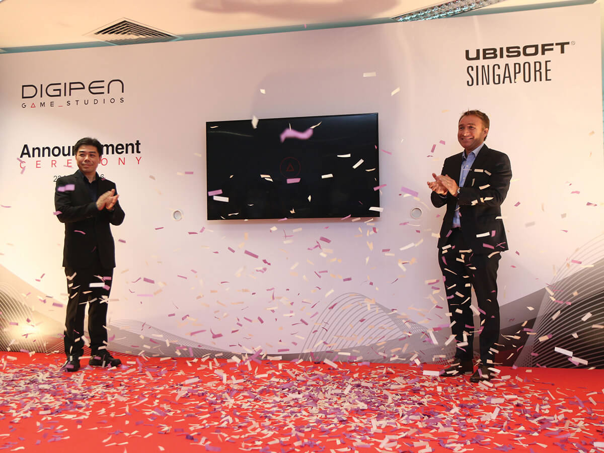 Jason Chu and Olivier de Rotalier applaud on stage as purple and white confetti falls. DigiPen and Ubisoft logos are on a wall behind them