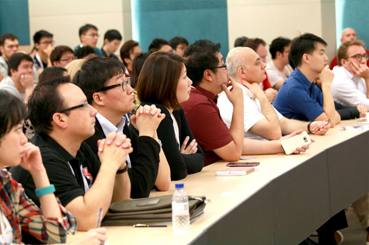 A group of industry professionals sit watching a presentation attentively behind a long countertop