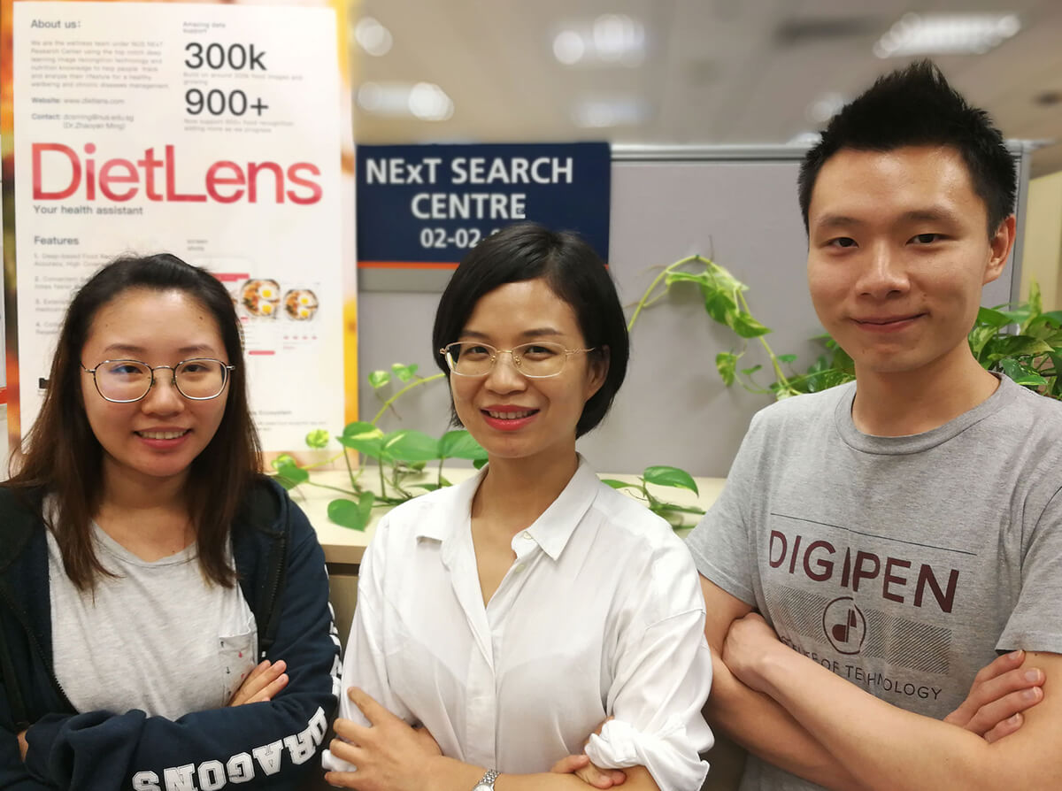 DigiPen (Singapore) alumni Irene Tan and Lim Sing Gee pose with a coworker in front of a DietLens banner 