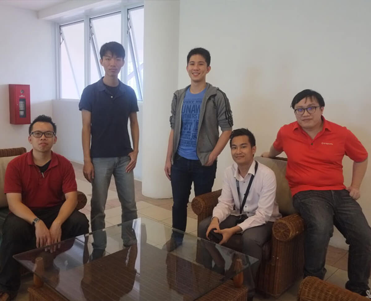 Five DigiPen graduates pose for a photo standing or sitting in a lobby with a glass table