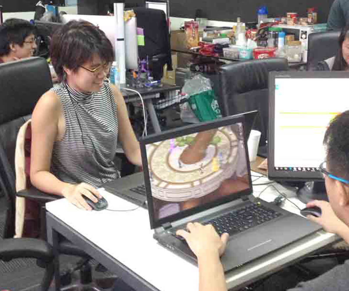 DigiPen graduates working on the game Masquerada at their laptops while seated at a desk
