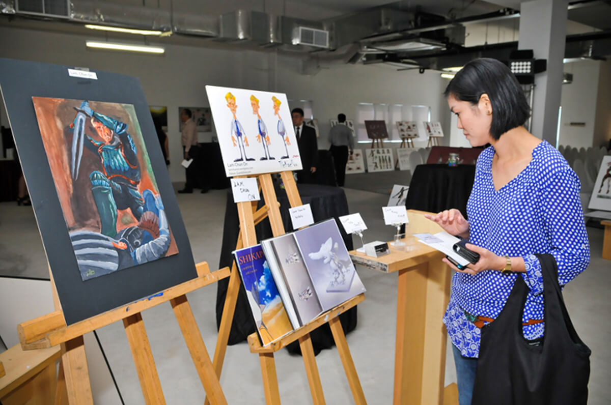 A visitor looks at the paintings, renderings, and other artwork displayed on two easels