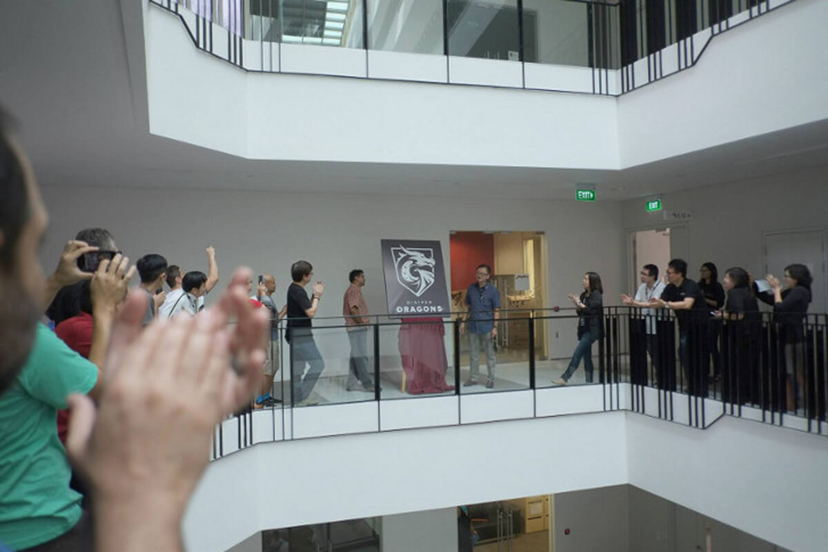 People crowd around the second story atrium as a poster with the DigiPen Dragon mascot is revealed on an easel