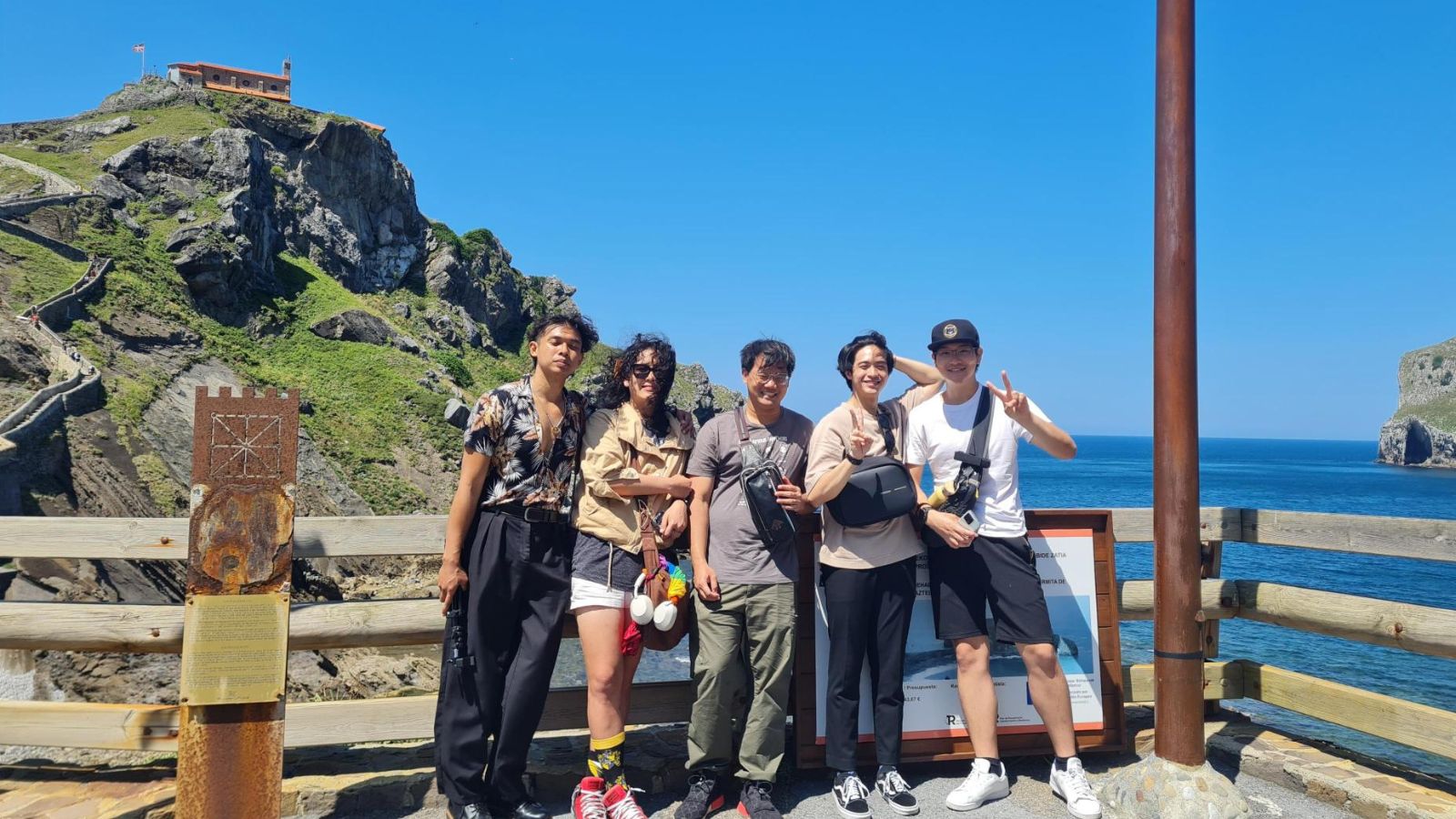 A group of five students pose near a scenic rock mountain near water