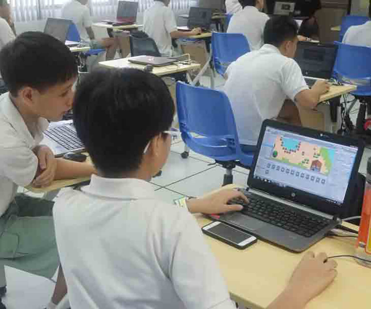 Laptop seen over the shoulder of a young student seated at desk working on a video game project