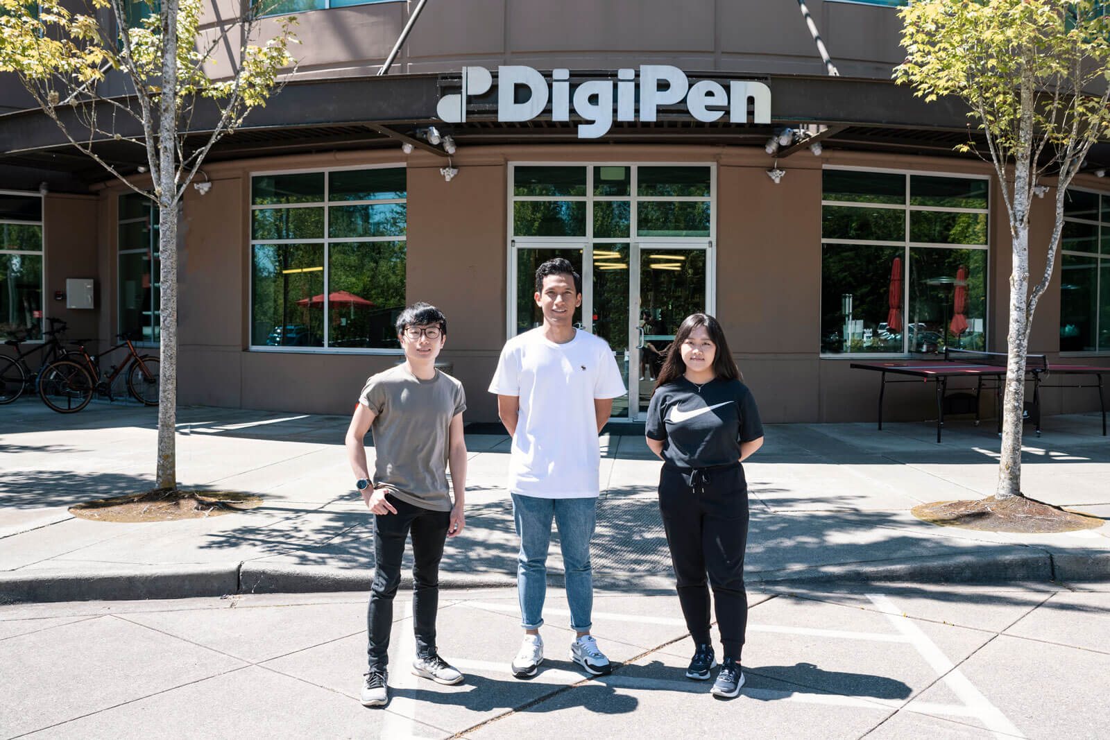 Three OIP students stand in front of the main doors of the DigiPen Redmond campus.