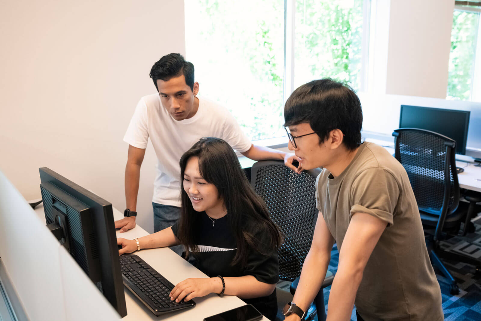 Three students look at the same computer screen in a computer lab.