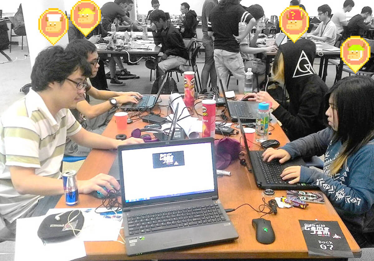 Four students sit at laptops working on their game; pixel-art oxen appear above each team member's head