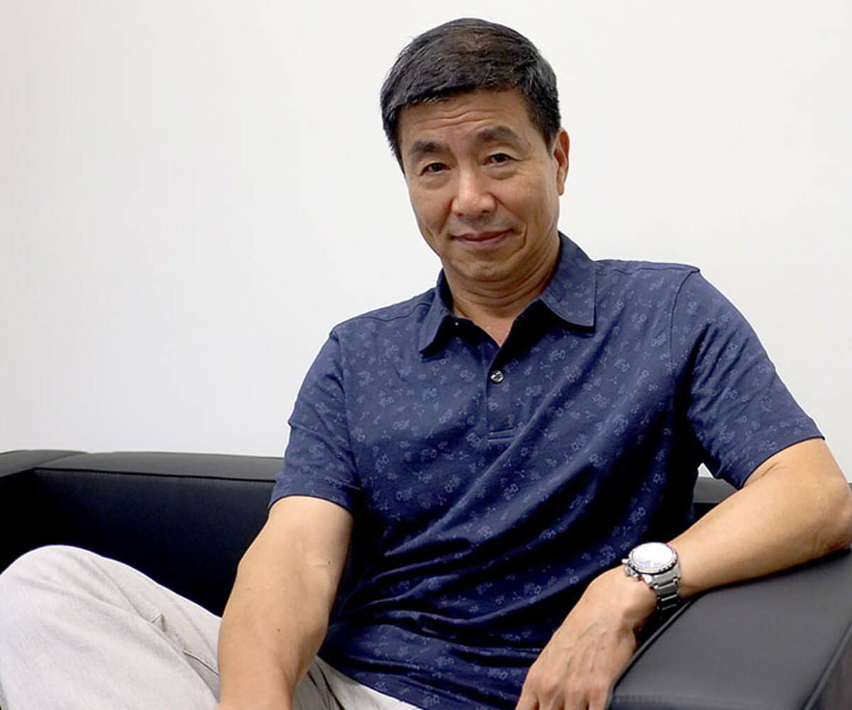 Dr. Xin Li poses for a photo sitting on a black couch