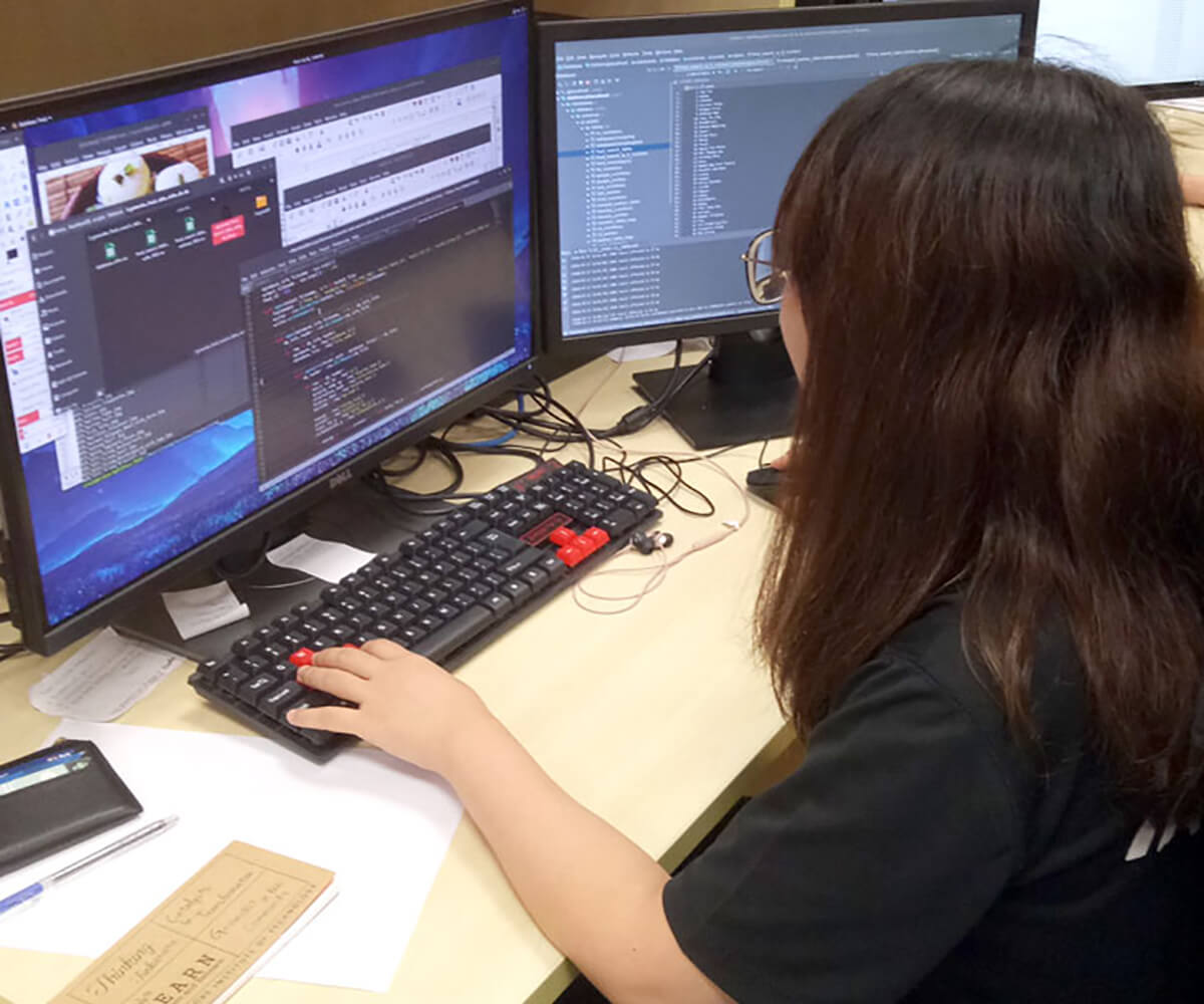 DigiPen (Singapore) BS in RTIS alumnae Irene Tan works at a desk in front of 2 monitors