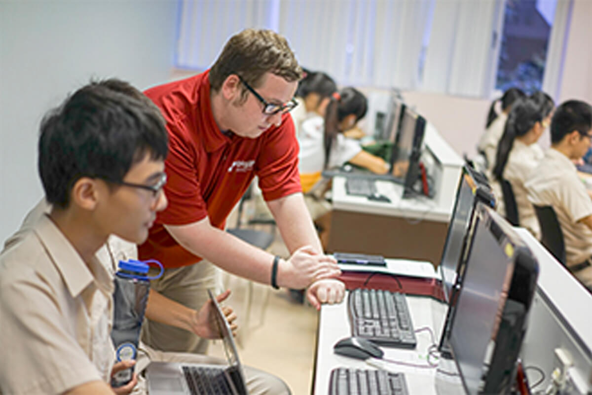 Instructor John Doran leans over to instruct a student at a computer desk