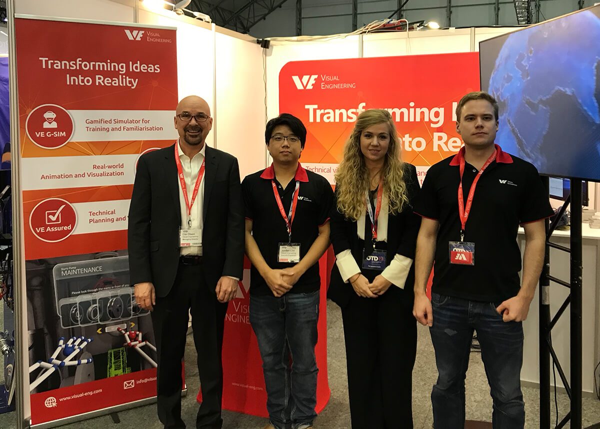 4 Visual Engineering employees stand parallel together facing camera in front of a company booth at an expo event.