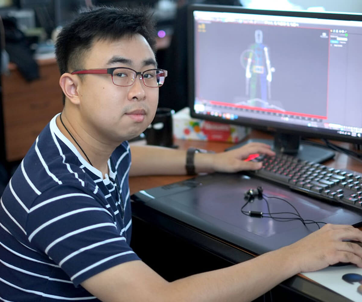 DigiPen graduate Lauri Gui poses for a photo at a desk with a monitor and tablet