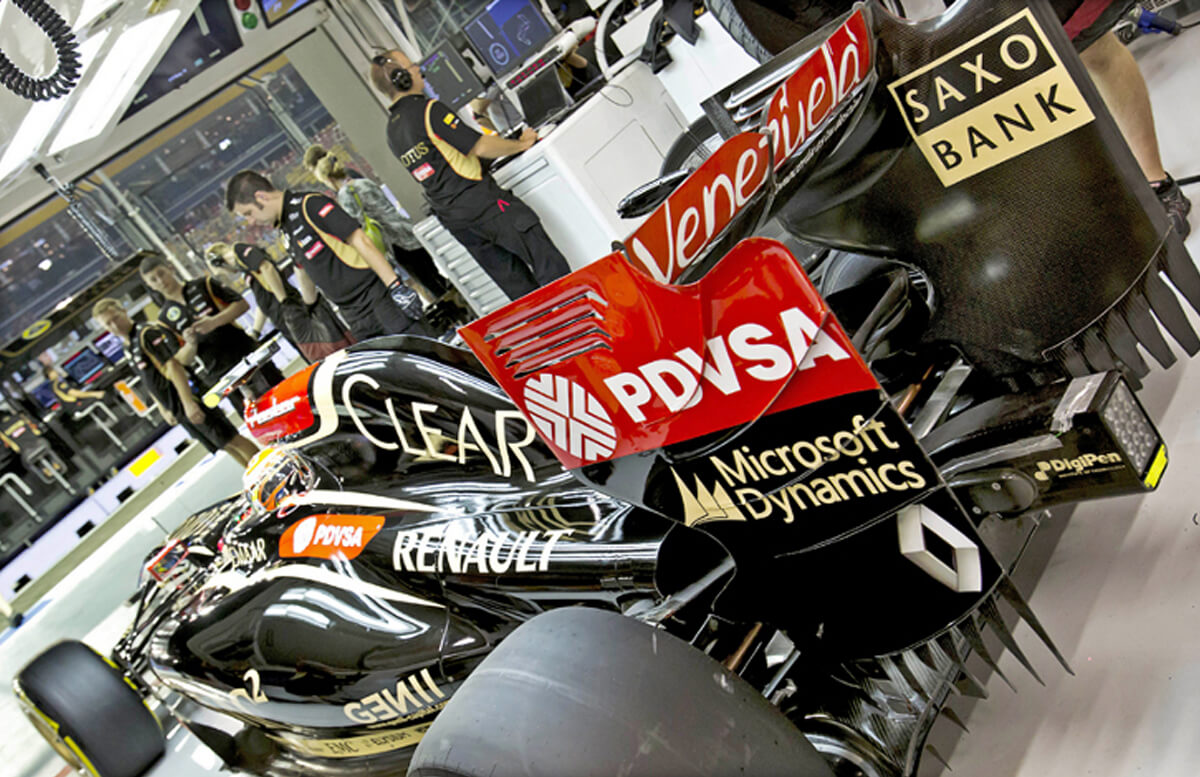 A shot of a black F1 race car from the rear surrounded by teammates, and emblazoned with several logos, including DigiPen