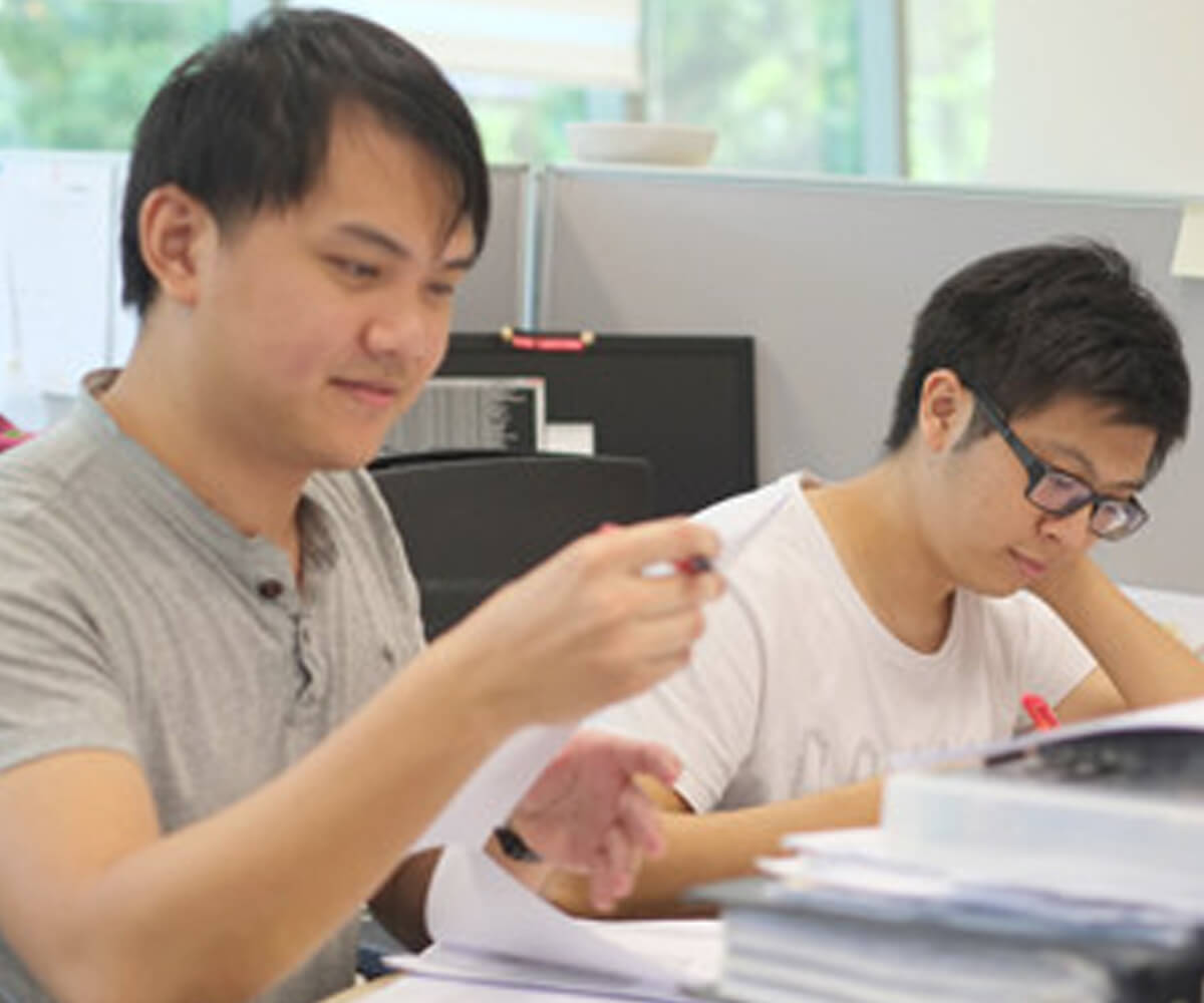 Graduates Michael Tay and Julian Teh sit at a desk reading papers