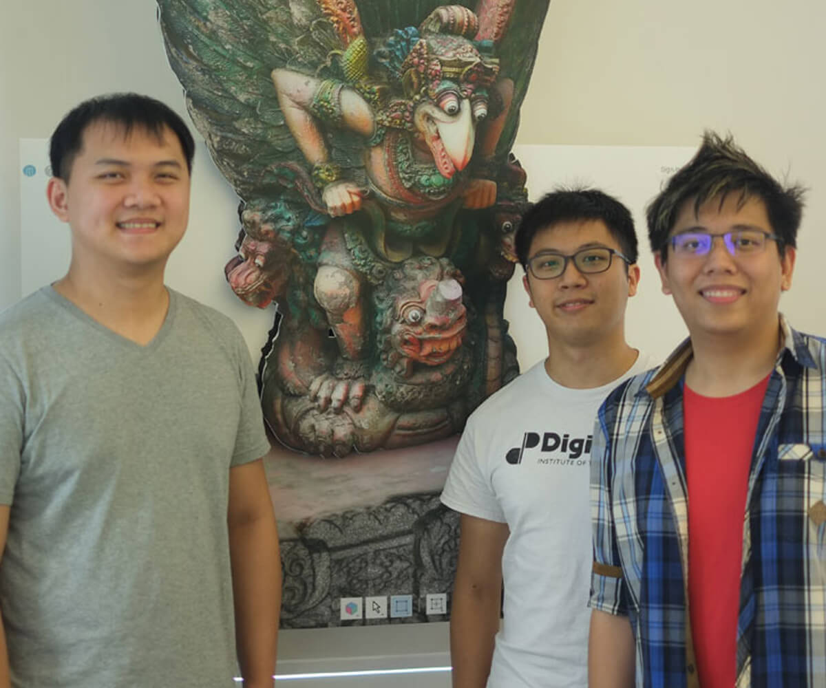 Graduates Michael Tay, Julian Teh, and Koh Naimin pose in front of an ornate cutout in the style of Southeast Asian sculpture