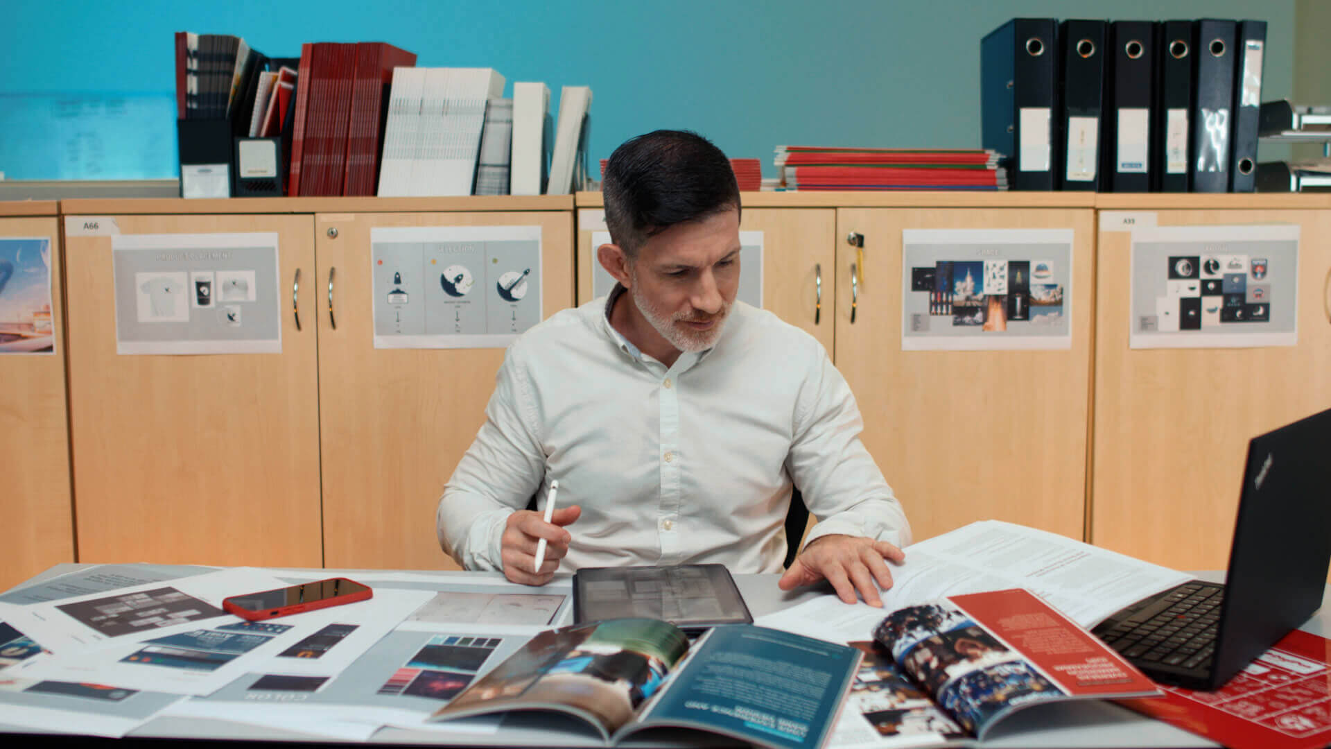 Michael Thompson sits at desk holding a stylus while looking at various magazines