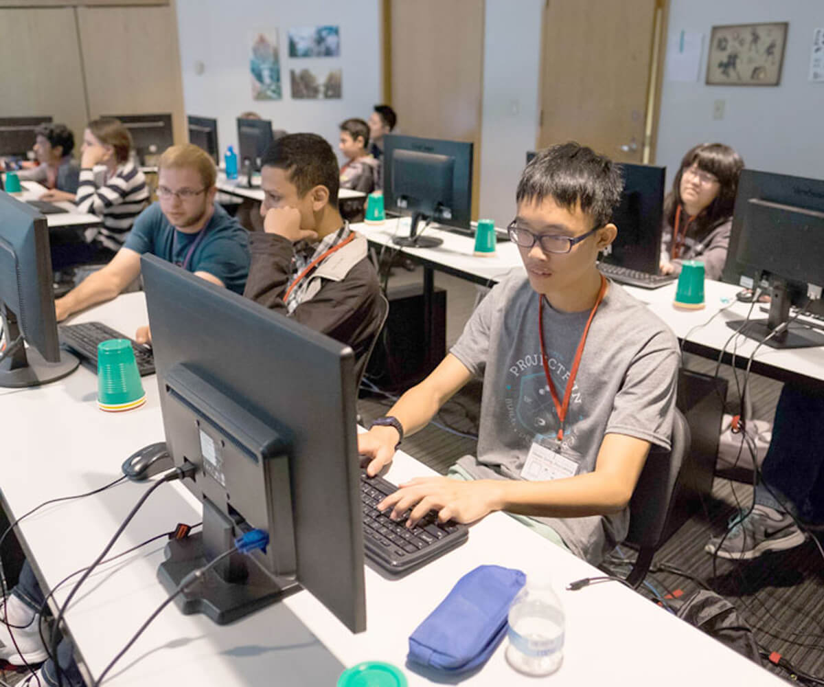 Several students each work at desks in a classroom looking at their computer monitors